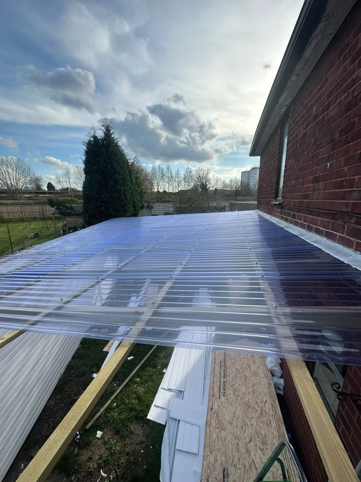 Clear polycarbonate roof sheets on a terrace beside a brick wall